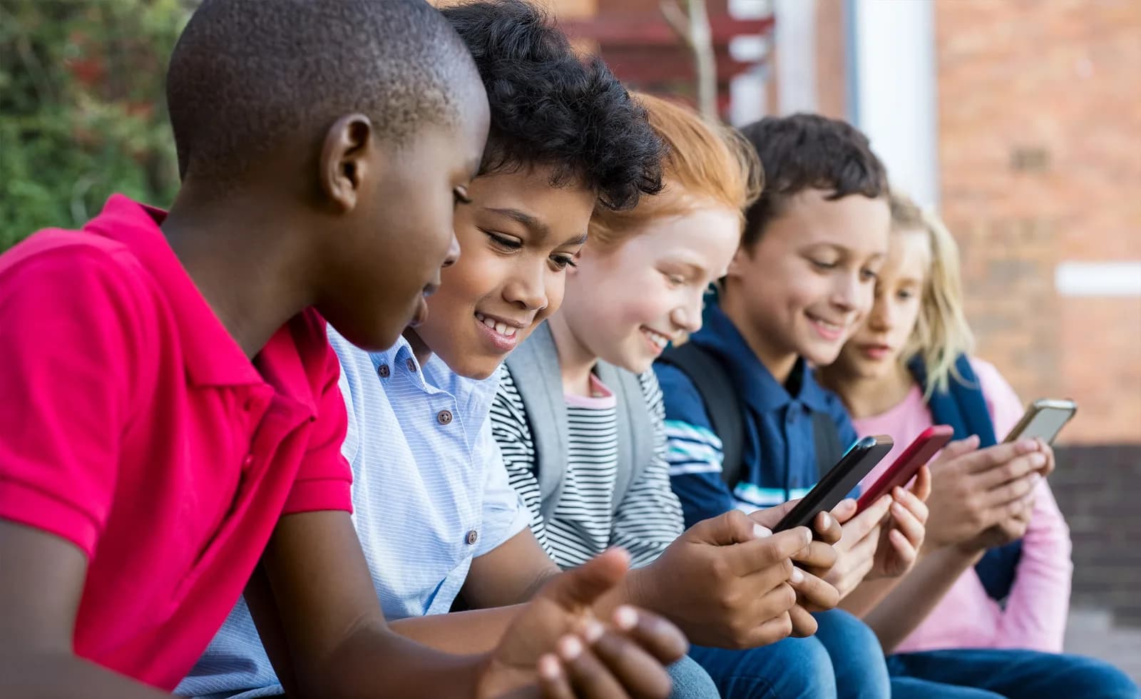 Grupo de crianças e adolescentes sentados juntos usando smartphones.