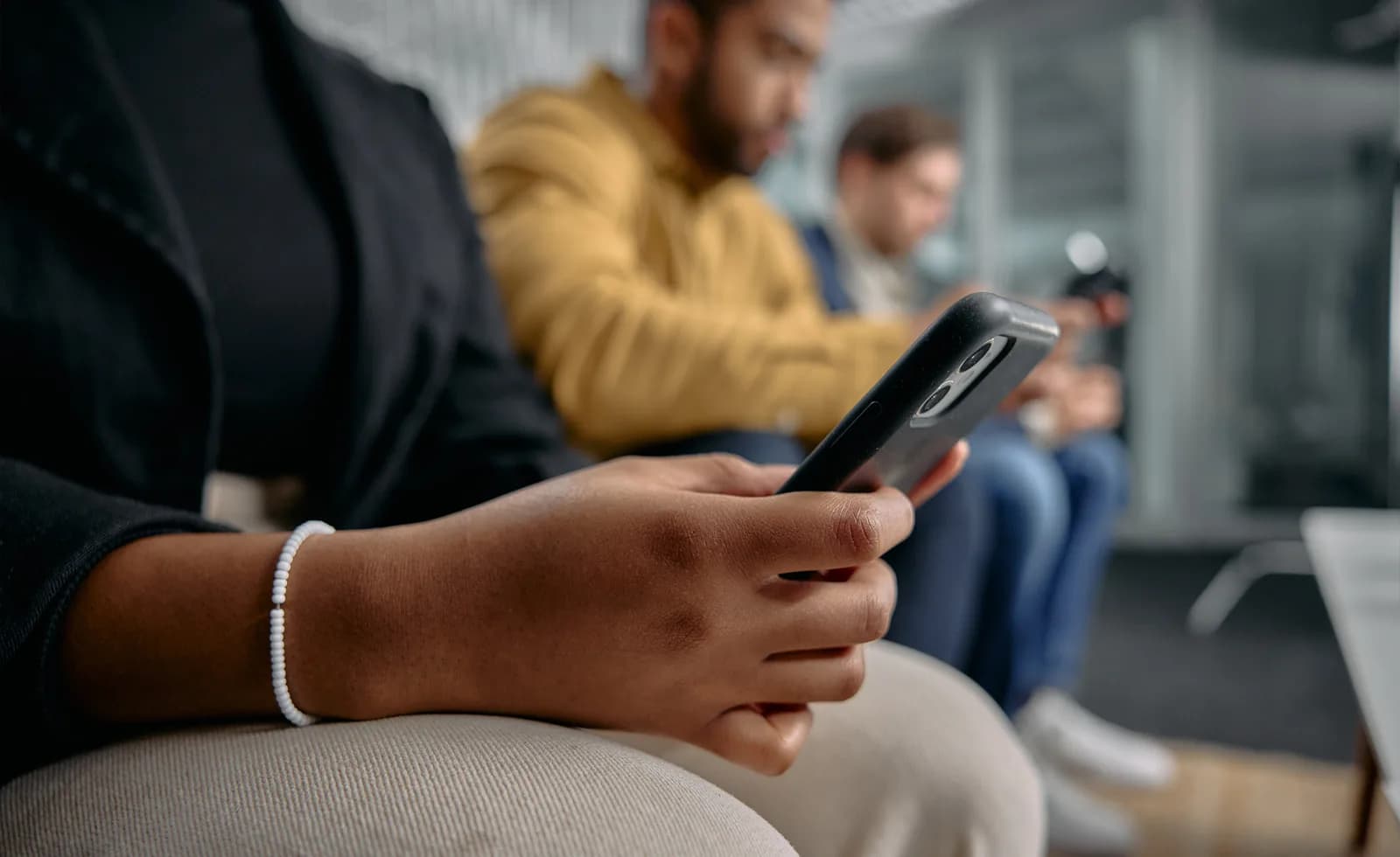 Pessoa usando smartphone em um ambiente com outras pessoas ao fundo.