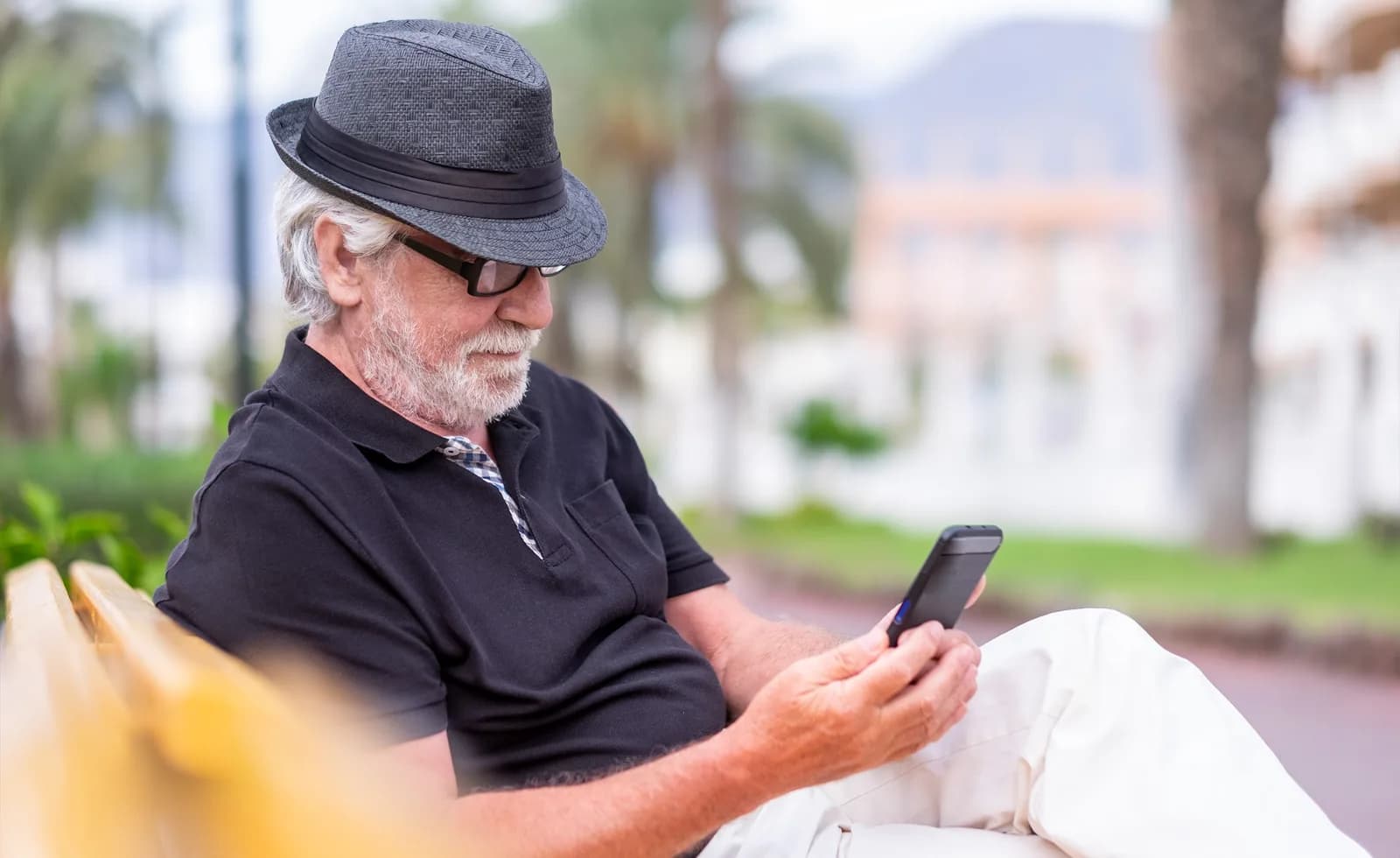 Homem idoso usando smartphone sentado ao ar livre.